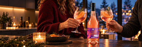 WinterPulle Pink Spritz mit winterlichen Rosé-Cocktails und zwei Erwachsenen beim gemeinsamen Anstoßen. KI-generiertes Stimmungsbild mit Originalflasche; Serviervorschlag.