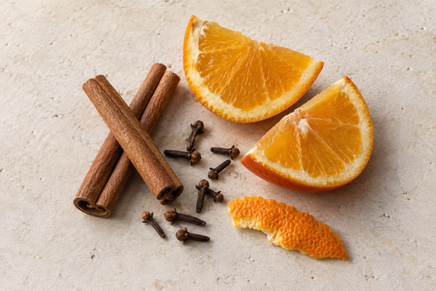 Zimtstangen, ganze Nelken, frische Orange und Orangenschale auf hellem Untergrund
